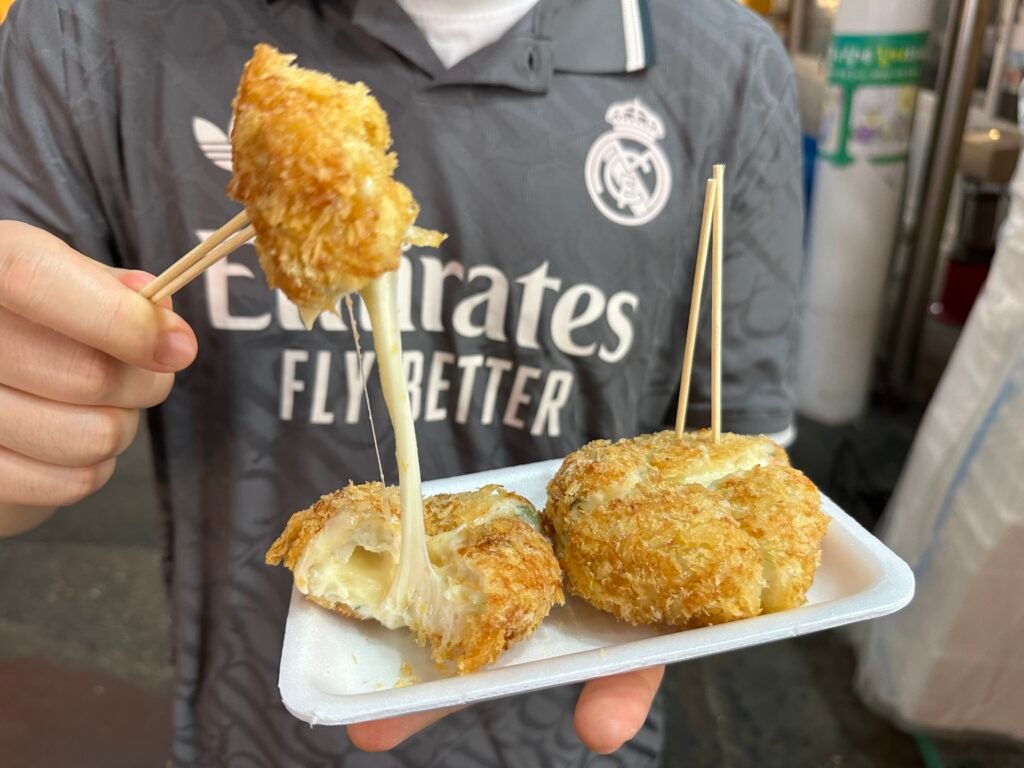 A piece of handmade fish cake croquette being lifted, with melted cheese stretching