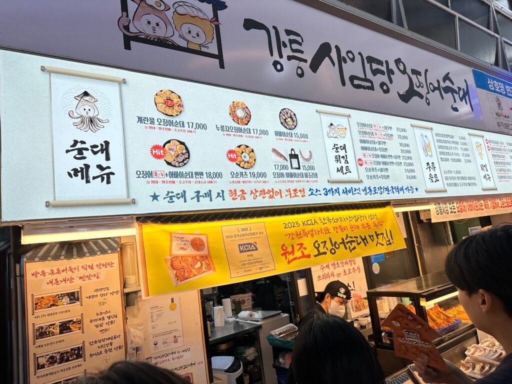 A white sign reading “Gangneung Saimdang Squid Sundae,” with various menu items listed below