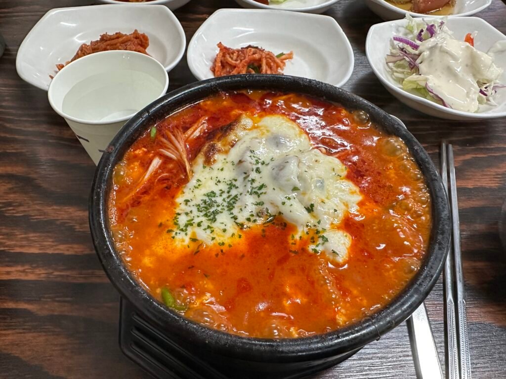 Cheese Jjolmyeon Sundubu served in a hot stone pot with red spicy broth and melted cheese