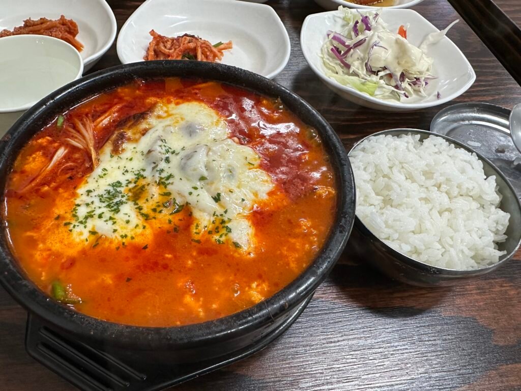 Cheese Jjolmyeon Sundubu with melted cheese served alongside a bowl of steamed rice