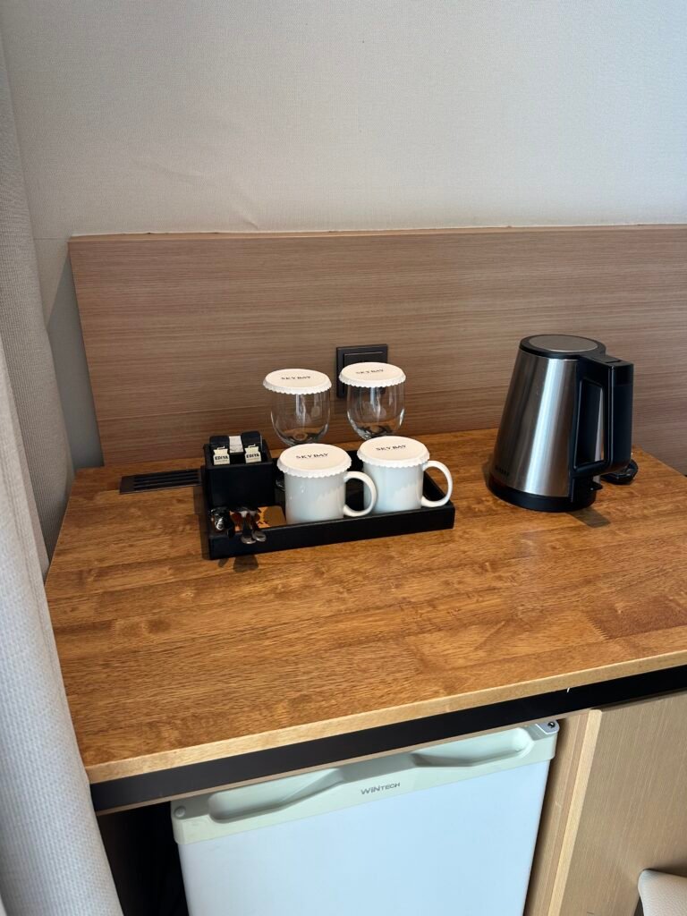Cups, wine glasses, a coffee kettle, and a mini fridge arranged in the hotel room