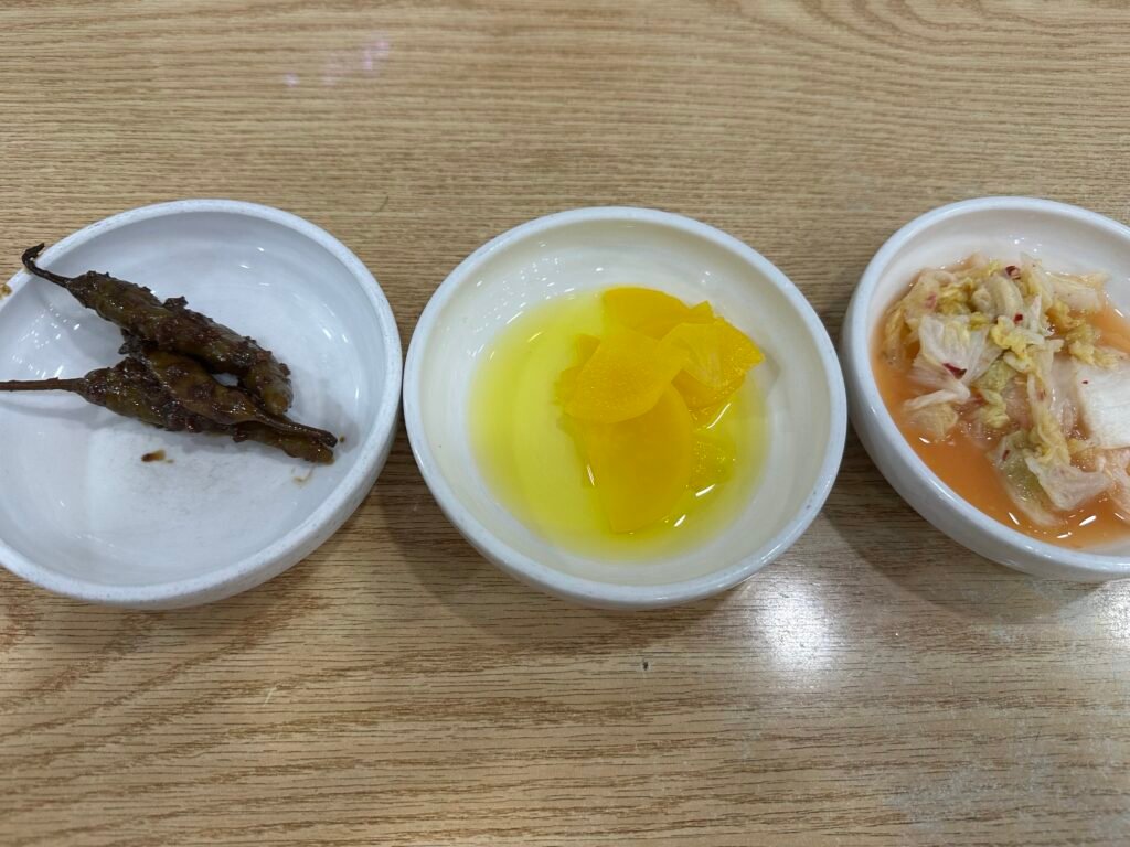 Three side dishes including chili pepper pickles, pickled radish, and white kimchi
