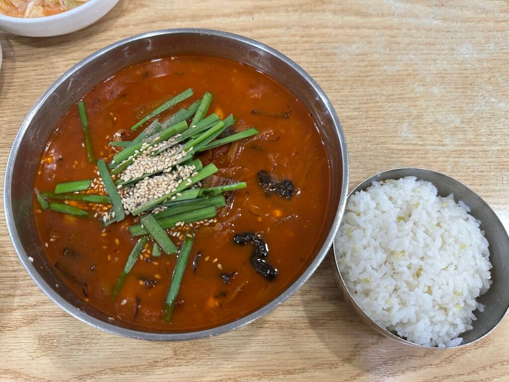 Jjamppong sundubu with rich red broth garnished with chives and sesame seeds, served with a bowl of white rice