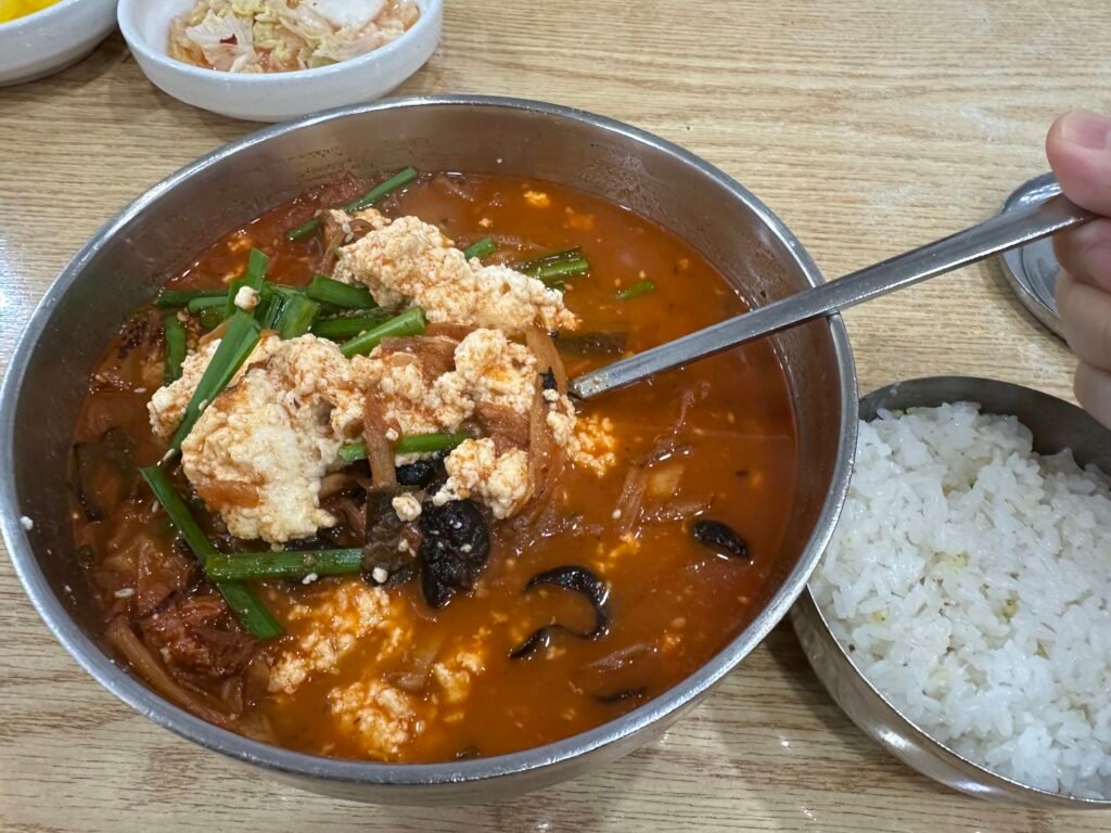Jjamppong sundubu with soft tofu lifted by a spoon from the rich red broth