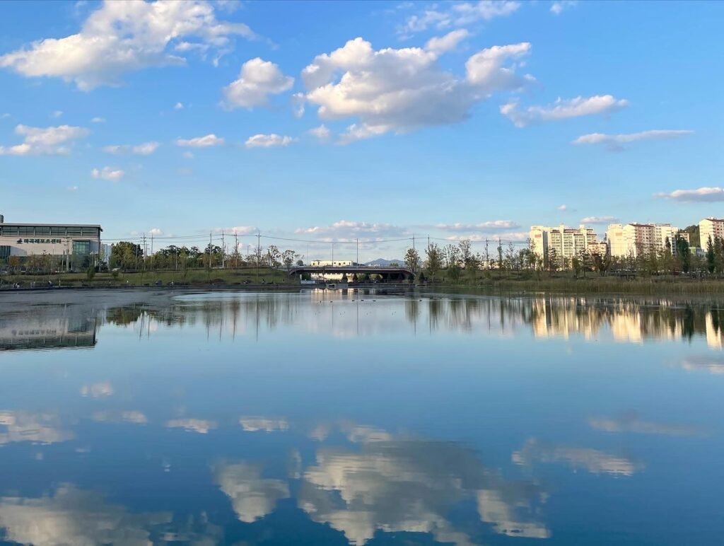 A calm, clear lake reflecting the blue sky and scattered clouds, forming a beautiful mirror-like scene