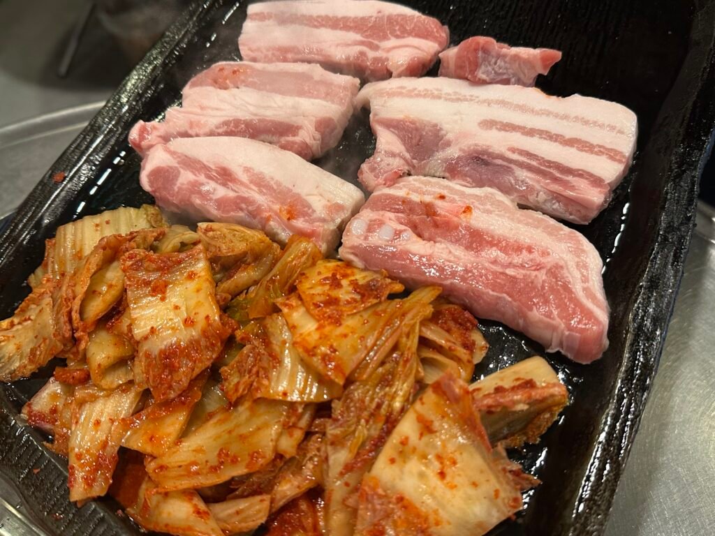 Fresh pork with pink and white marbling served alongside red, savory-looking stir-fried kimchi